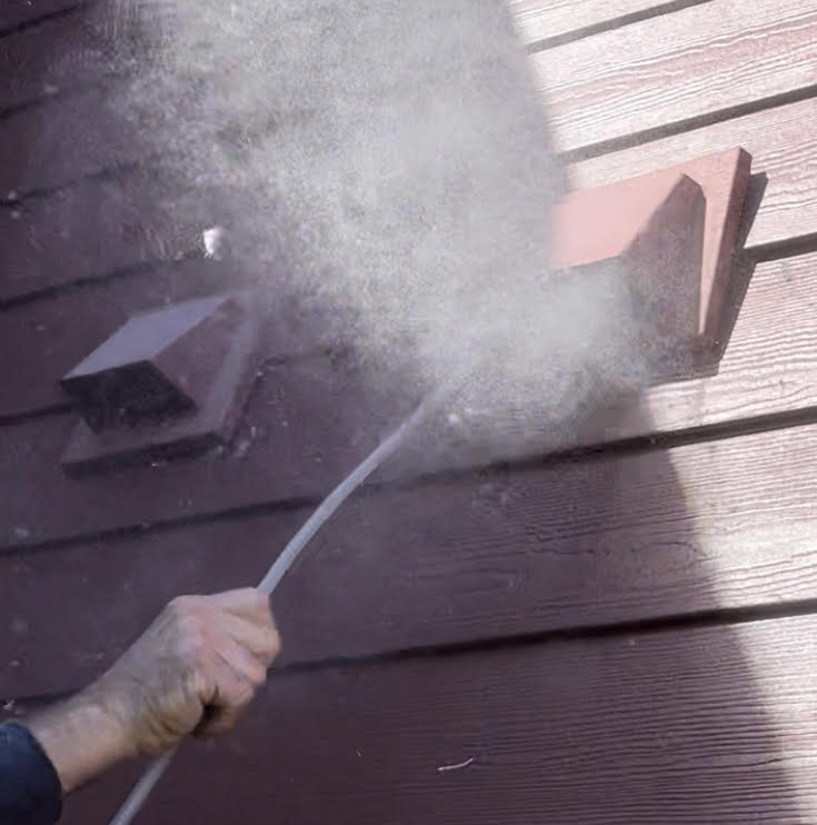 Technician blowing built-up lint out of an exterior dryer vent