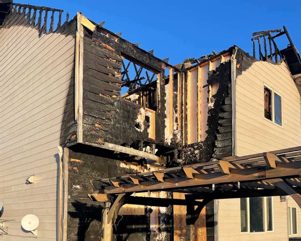 Fire-damaged two-story home with charred siding and burned roof framing